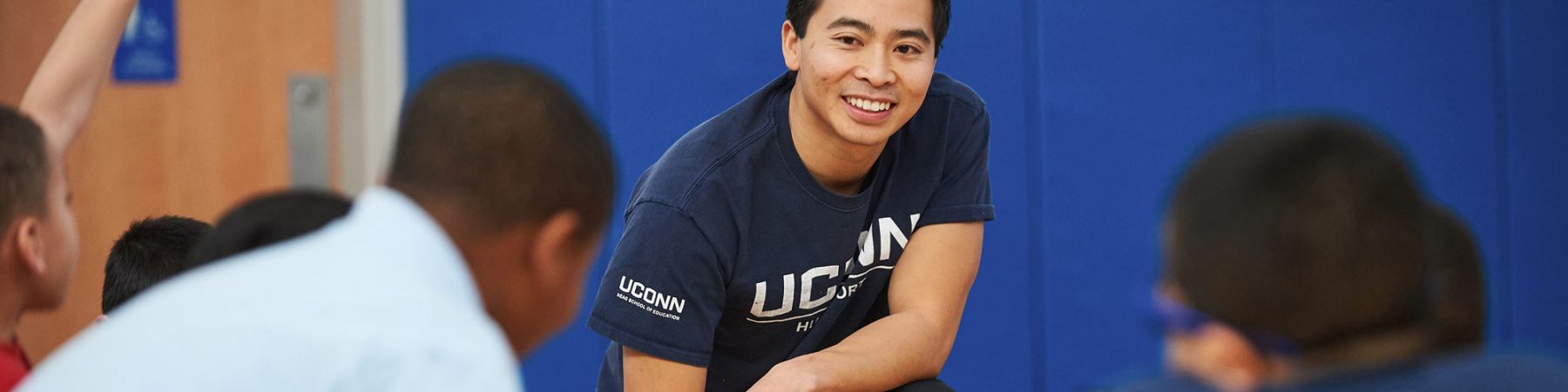 Jesse Mala on his knee with Husky Sport: UConn Online Graduate Certificate in Leadership and Sport Management